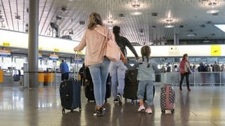 Eine Familie mit Kind am Flughafen. Hier ist es im Urlaub besonders sinnvoll, bei der Auslandskrankenversicherung genau hinzuschauen.