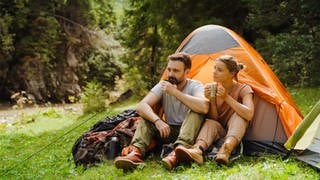 Junges Paar beim Camping in einem Zelt, umgeben von idyllischer Natur. Symbolbild: Tipps fürs Camping für Anfänger mit Checkliste und Packliste.