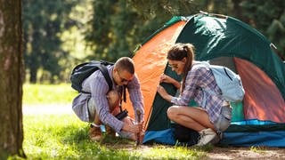 Junges Paar beim Camping in einem Zelt, umgeben von idyllischer Natur. Symbolbild: Tipps fürs Camping für Anfänger mit Checkliste und Packliste.