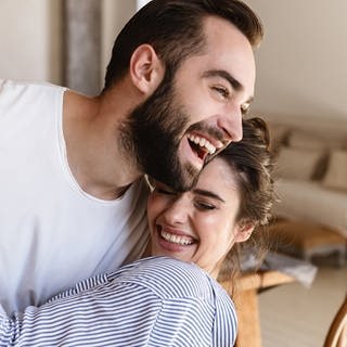 Junges Paar tanzt verliebt durch die Wohnung. Symbolbild für Tipps für eine glückliche Beziehung und lange Liebe.