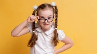 Mädchen mit Zöpfen und einer Brille sieht sehr schlau aus. Symbolbild für Merksätze und Eselsbrücken gegen Fehler in der deutschen Rechtschreibung.