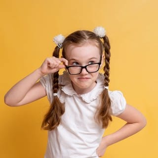 Mädchen mit Zöpfen und einer Brille sieht sehr schlau aus. Symbolbild für Merksätze und Eselsbrücken gegen Fehler in der deutschen Rechtschreibung.