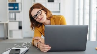 Junge Frau sitzt in einem Büro an einem Laptop. Symbolbild für häufige Schreibfehler in E-Mails und die richtige Lösung laut Duden für Grußformeln und Kommasetzung.