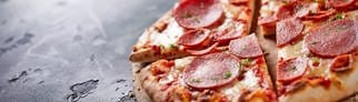 Eine Salami-Tiefkühlpizza auf einem Holzbrett und schwarzem, steinernen Untergrund. Stiftung Warentest hat 21 Tiefkühlpizzen auf Geschmack, ernährungsphysiologische Merkmale und weiteren Kriterien getestet.