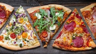 Mehrere Stücke Tiefkühlpizza liegen nebeneinander. Sie sind alle unterschiedlich. Welche Tiefkühlpizza ist die beste? Stiftung Warentest hat Salami-Pizza aus der Tiefkühltruhe getestet.