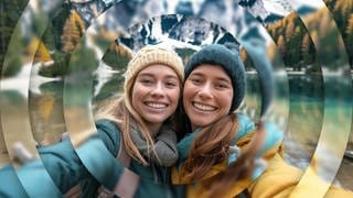 Zwei junge Frauen machen ein Selfie vor Bergen in Südtirol, ein Urlaub in traumhafter Natur.