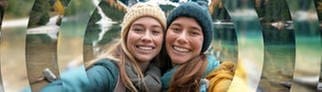 Zwei junge Frauen machen ein Selfie vor Bergen in Südtirol, ein Urlaub in traumhafter Natur.