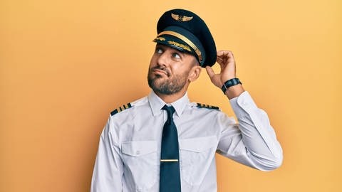 Junger Mann im Piloten-Outfit, kratzt sich denkend am Kopf. Symbolbild für ein Quiz mit lustigen Umschreibungen für verschiedenen Berufe.