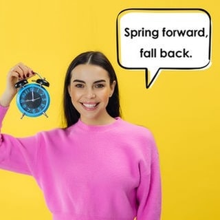 Eine junge Frau hält einen Wecker hoch und lächelt. Der Wecker zeigt 9:00 Uhr als Uhrzeit an. In einer Sprechblase neben ihr steht: „Spring forward, fall back.“ Symbolbild für Merksätze bzw. Eselsbrücken und Merksätze in andern Sprachen, um sich leichter zu merken, in welche Richtung die Uhr bei der Zeitumstellung gestellt werden muss. 