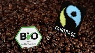 Das EG-Biosiegel und das Fairtrade-Siegel liegen auf Kaffeebohnen. Symbolbild für einen Test bei Stiftung Warentest in dem 15 Filterkaffees sind