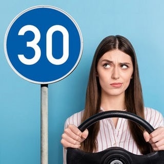 Junge Frau sitzt denkend hinter dem Lenkrad und schaut auf ein blaues Verkehrsschild mit weißer Schrift. Symbolbild für unbekannte Verkehrsschilder in Deutschland und ihre Bedeutung für Autofahrer.