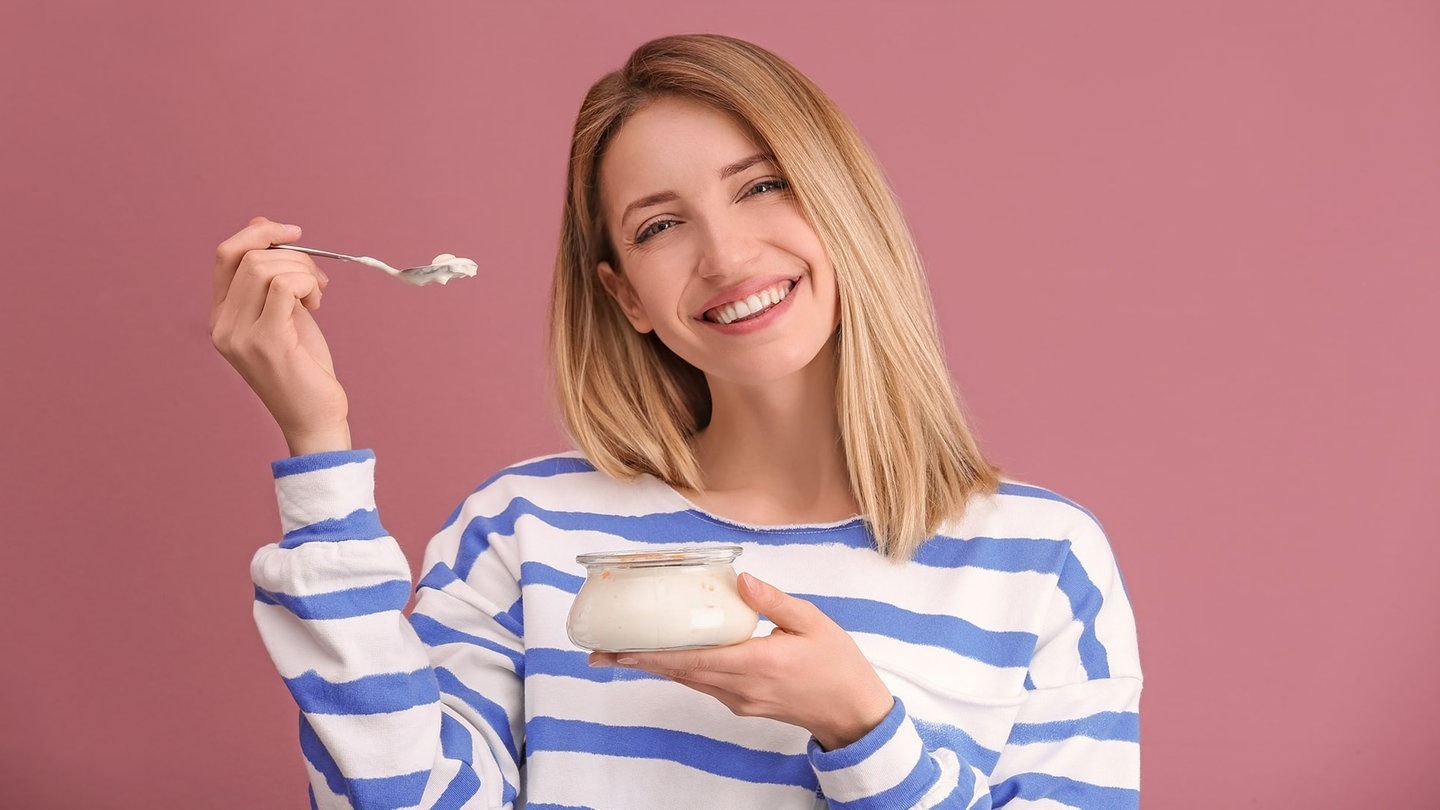 Junge Frau löffelt mit fragendem Blick einen Joghurt aus. Symbolbild fürs Grammatik-Quiz: Welcher Artikel ist in der deutschen Sprache richtig?