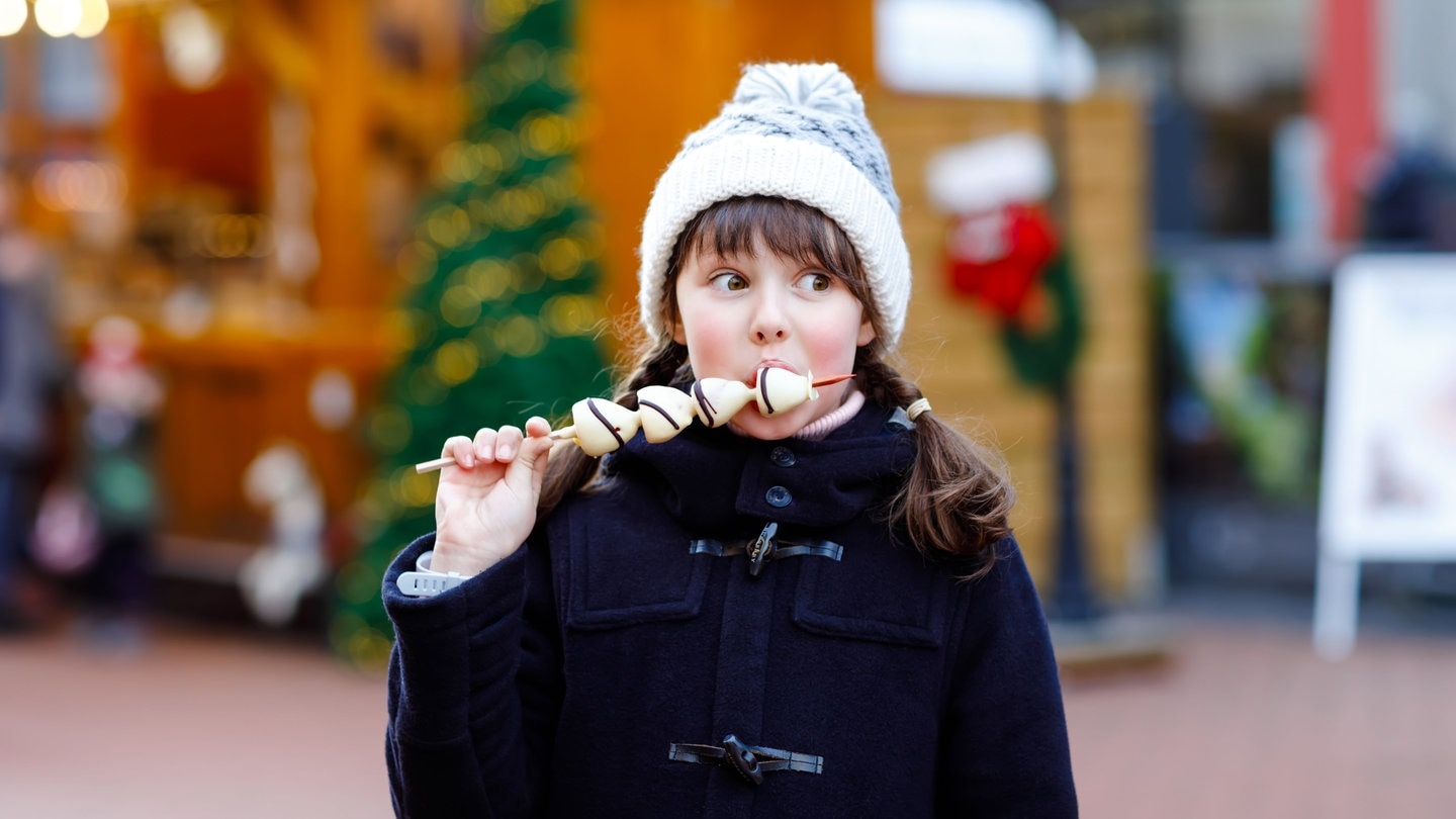 Mädchen isst Schokofrüchte auf einem Weihnachtsmarkt | Besondere Weihnachtsmärkte in Baden-Württemberg und Rheinland-Pfalz