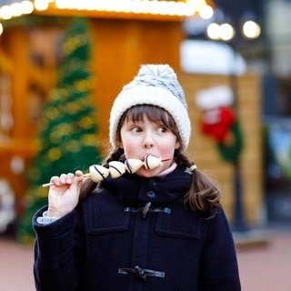 Mädchen isst Schokofrüchte auf einem Weihnachtsmarkt | Besondere Weihnachtsmärkte in Baden-Württemberg und Rheinland-Pfalz