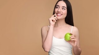 Frau mit Apfel in der hat nimmt Vitamin-D-Tablette ein | Symbolbild für Vitamin-D-Mangel und was die Symptome sind