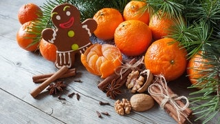 Mandarinen in einem Gedeck an Weihnachten auf dem Tisch mit Tannenzweigen und Lebkuchenmännchen. Symbolbild für den Unterschied zwischen Mandarine und Clementine.