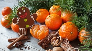 Mandarinen in einem Gedeck an Weihnachten auf dem Tisch mit Tannenzweigen und Lebkuchenmännchen. Symbolbild für den Unterschied zwischen Mandarine und Clementine.