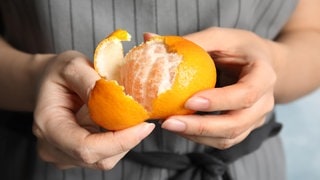 Hände schälen eine Mandarine. Symbolbild für den Unterschied zwischen Mandarine und Clementine.