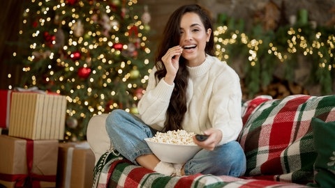 Eine Frau sitzt auf der Couch und sieht sich einen Weihnachtsfilm im Fernsehen an.