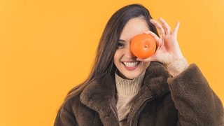 Junge Frau hält sich eine Mandarine vors Gesicht. Symbolbild für den Unterschied zwischen Mandarine und Clementine.