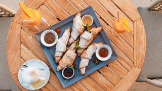 SWR3 Gewinnspiel: Gewinnerhotel in Montenegro. Ein Frühstück aus Croissants und Cocktails auf einem Holztisch in Tivat, Montenegro.