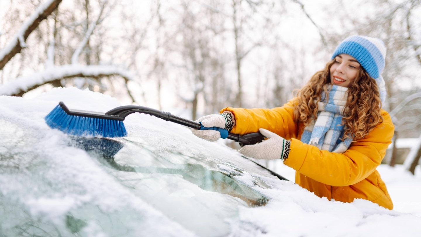 Junge Frau beim Eiskratzen: Die Autoscheibe ist im Winter auch von innen gefroren und vereist.