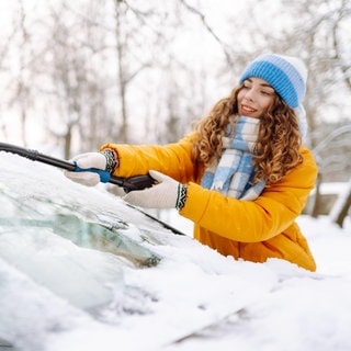 Junge Frau beim Eiskratzen: Die Autoscheibe ist im Winter auch von innen gefroren und vereist. 