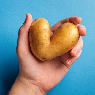 Hände halten eine herzförmige Kartoffel. Symbolbild für das Superfood Kartoffel – Vitamine, Ballaststoffe, Kalorien, und Rezepte