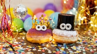 Zwei Berliner mit Augen auf einem Tisch mit Luftschlangen. Symbolbild für Traditionen an Silvester, kuriose Bräuche aus anderen Ländern zu Neujahr.