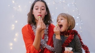 Zwei junge Frauen essen Trauben zu Silvester. Symbolbild für Bräuche und Traditionen in anderen Ländern.