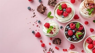 Viele kleine Desserts mit Beeren auf rosafarbenem Grund. Symbolbild zum Mythos Dessert-Magen: Warum geht ein Nachtisch oder Süßes immer noch rein, obwohl man satt ist?