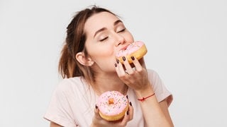 Junge Frau schaut hungrig auf ein Stück Torte. Symbolbild zum Mythos Dessert-Magen: Warum geht ein Nachtisch oder Süßes immer noch rein, obwohl man satt ist?