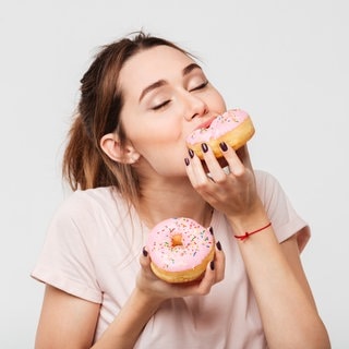 Junge Frau schaut hungrig auf ein Stück Torte. Symbolbild zum Mythos Dessert-Magen: Warum geht ein Nachtisch oder Süßes immer noch rein, obwohl man satt ist?