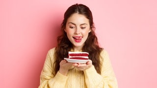 Junge Frau schaut hungrig auf ein Stück Torte. Symbolbild zum Mythos Dessert-Magen: Warum geht ein Nachtisch oder Süßes immer noch rein, obwohl man satt ist?