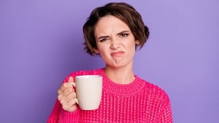 Junge Frau hält eine Kaffeetasse in der Hand und rümpft die Nase. Symbolbild für Tipps bei Schimmel in der Kaffeemaschine zum Reinigen und Vorbeugen.