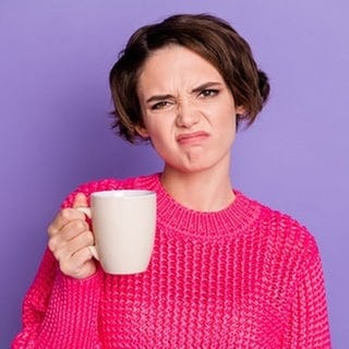 Junge Frau hält eine Kaffeetasse in der Hand und rümpft die Nase. Symbolbild für Tipps bei Schimmel in der Kaffeemaschine zum Reinigen und Vorbeugen.