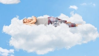 Junge Frau liegt auf Wolken und schläft. Symbolbild für den Selbsttest optimale Schlafdauer: Sind 6 Stunden Schlaf genug?