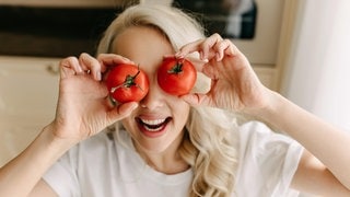 Frau hält sich Tomaten über die Augen. Symbolbild für das SWR3 Quiz zu Redewendungen: „Hast du Tomaten auf den Augen?“