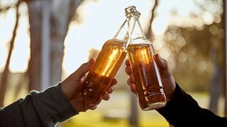 Zwei Männer stoßen mit Bierflaschen an. Auch alkoholfreies Bier kann bis zu 0,5 Prozentvolumen Alkohol enthalten.