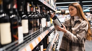 Eine Frau prüft das Etikett einer Flasche Wein im Supermarkt. In alkoholfreien Getränken kann Alkohol enthalten sein.