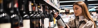 Eine Frau prüft das Etikett einer Flasche Wein im Supermarkt. In alkoholfreien Getränken kann Alkohol enthalten sein.