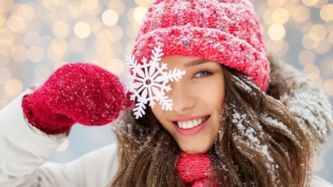 Eine Frau hält eine Schneeflocke vor ihr Auge und freut sich, dass das Bergwetter gut ist