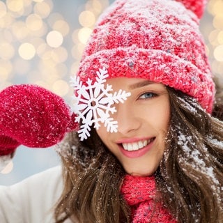 Eine Frau hält eine Schneeflocke vor ihr Auge und freut sich, dass das Bergwetter gut ist