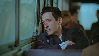 Filmszene aus „Der Brutalist“. Schauspieler Adrian Brody sitzt in einem Bus und schaut aus dem Fenster. Der Film ist für zehn Oscars nominiert, hier liest du unsere Filmkritik.