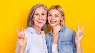 Boomer-Mutter und jüngere Tochter lächelnd nebeneinander mit „Peace“-Handzeichen. Symbolbild für typische Wörter, die vor allem Boomer benutzen – und in der Sprache anderer Generationen eher keine Rolle spielen.