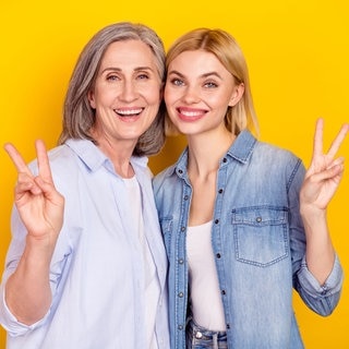 Boomer-Mutter und jüngere Tochter lächelnd nebeneinander mit „Peace“-Handzeichen. Symbolbild für typische Wörter, die vor allem Boomer benutzen – und in der Sprache anderer Generationen eher keine Rolle spielen.