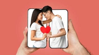 Ein Paar, das sich über zwei Smartphones hinweg mit Herz in der Hand umarmt. Symbolbild für lustige und kitschige Whatsapp-Sprüche und Grüße zum Valentinstag.