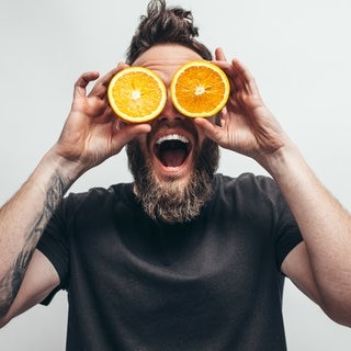 Ein Mann hält sich jeweils eine Orangenhälfte vor die Augen | Vitamin C & Zink bei Erkältung