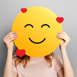 Frau hält sich ein Emoji mit Herzen vors Gesicht. Symbolbild für Dialekt-Wörter aus deutschen Dialekten, die wir lieben – ein Best-of aus der SWR3 Morningshow.