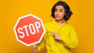 Junge Frau mit Stopp-Schild. Symbolbild für clevere Sprüche, um ein Gespräch zu beenden, bevor es zum Streit kommt.